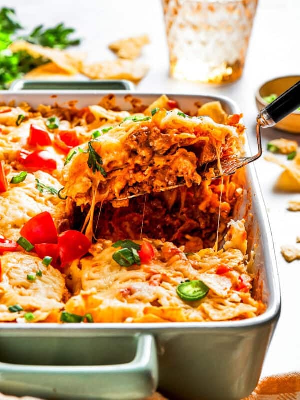 A serving spoon lifting out a slice of Dorito casserole from a baking dish.