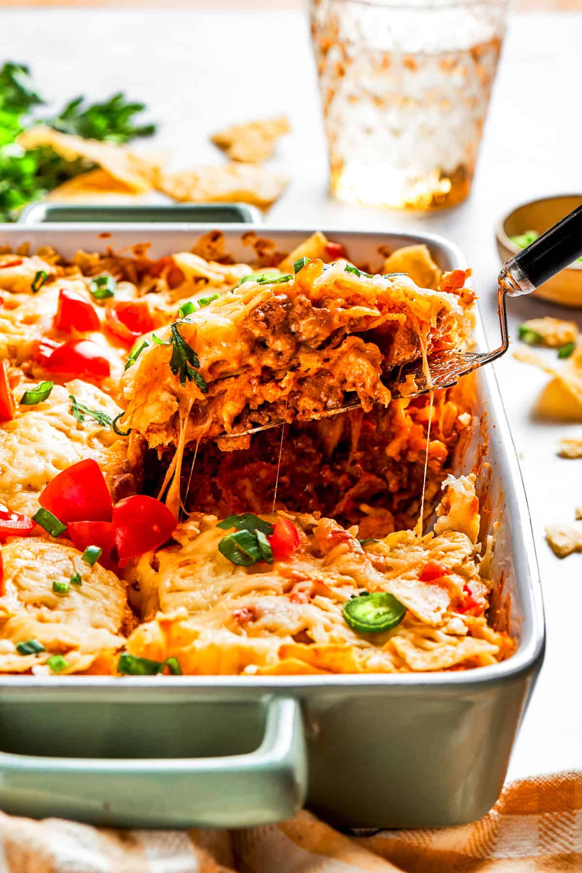 A serving spoon lifting out a slice of Dorito casserole from a baking dish.