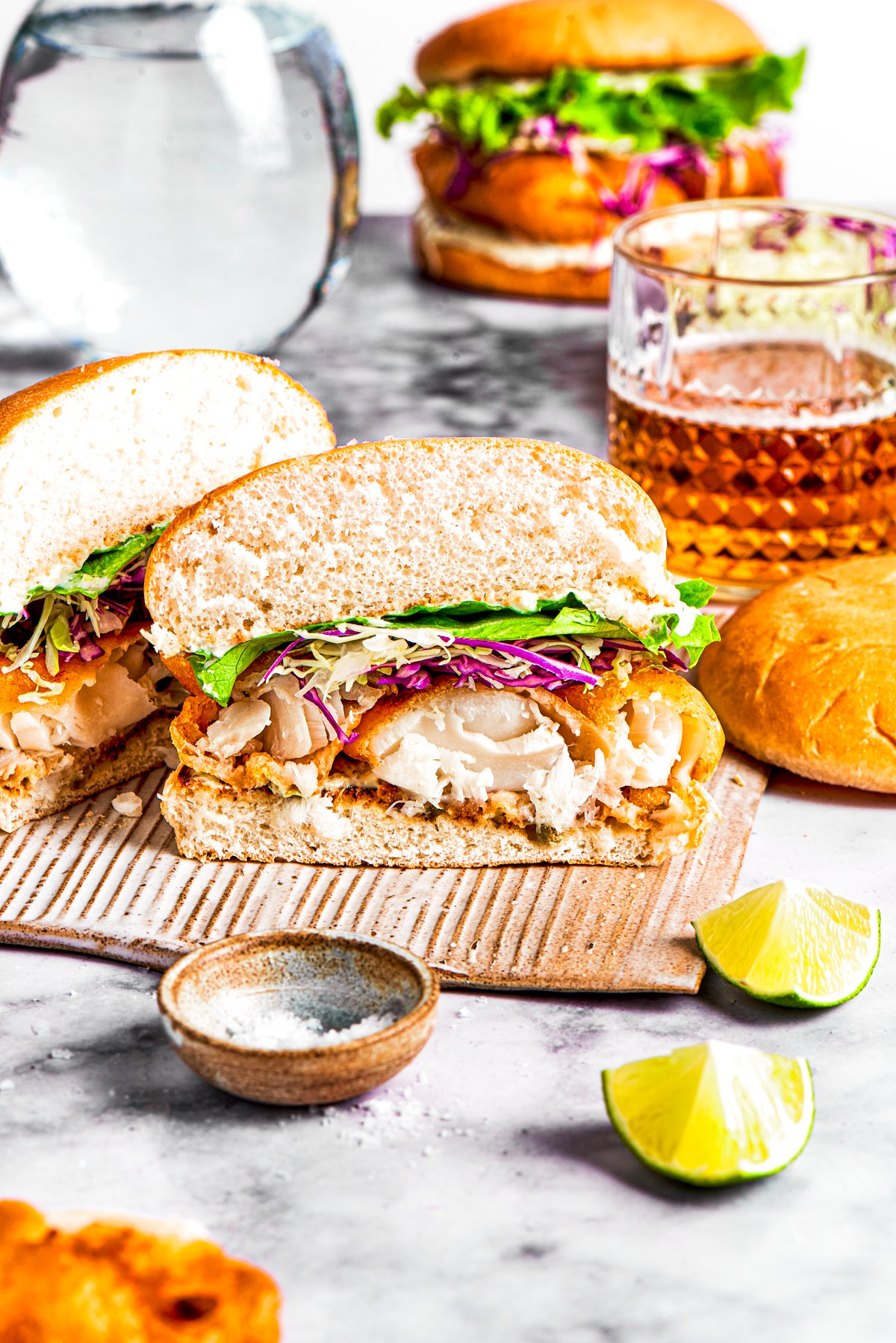 A fish sandwich cut in half and facing the camera so the contents of the sandwich are visible.