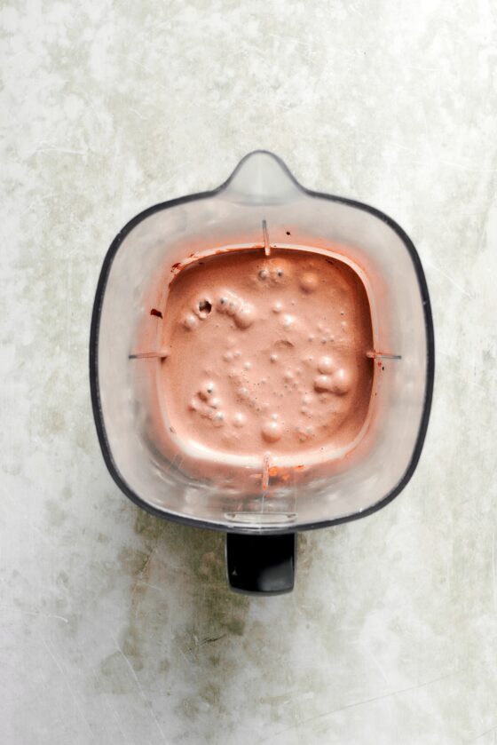 A blender holds a blended chocolate milkshake.