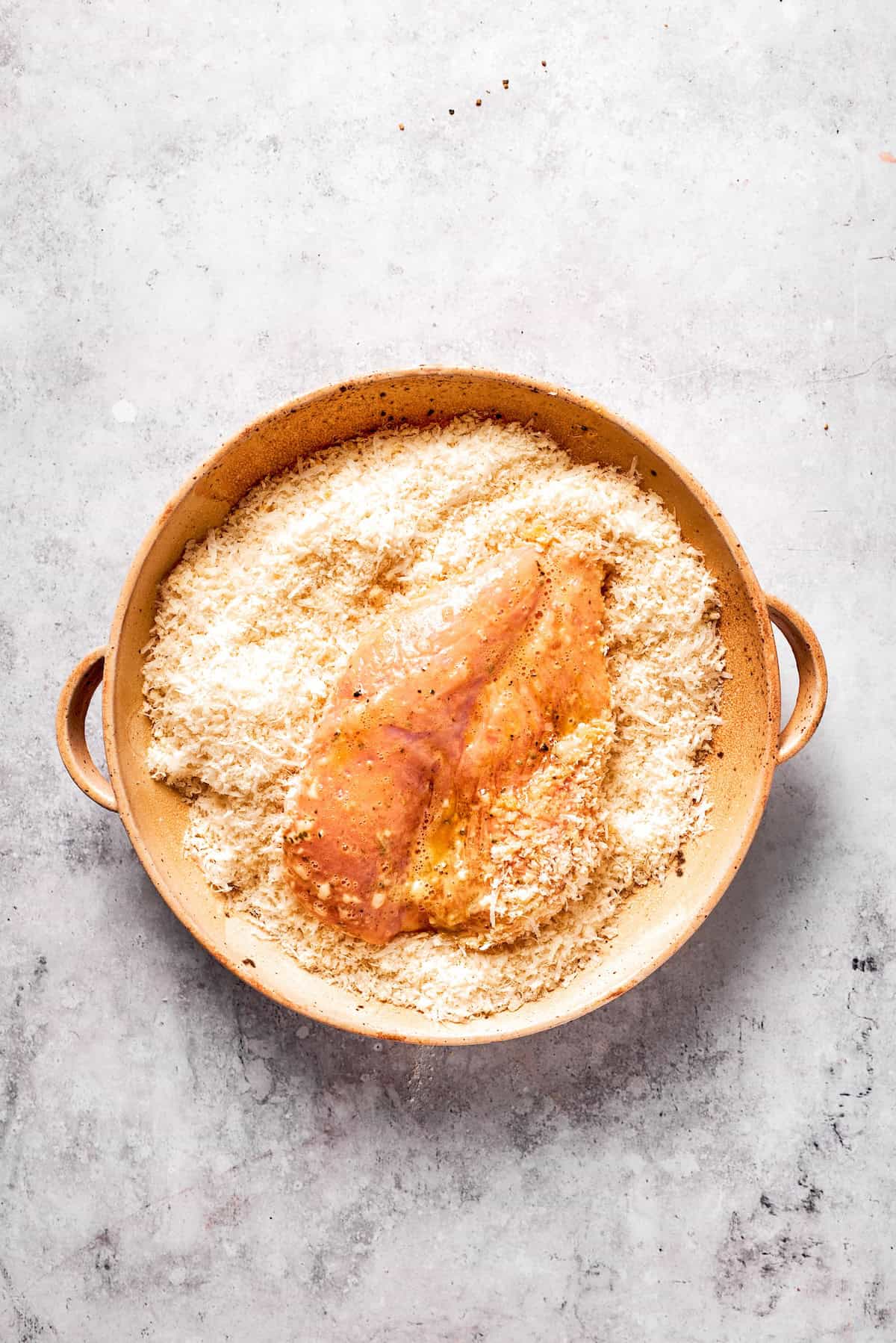A piece of chicken is placed in a breadcrumb mix.