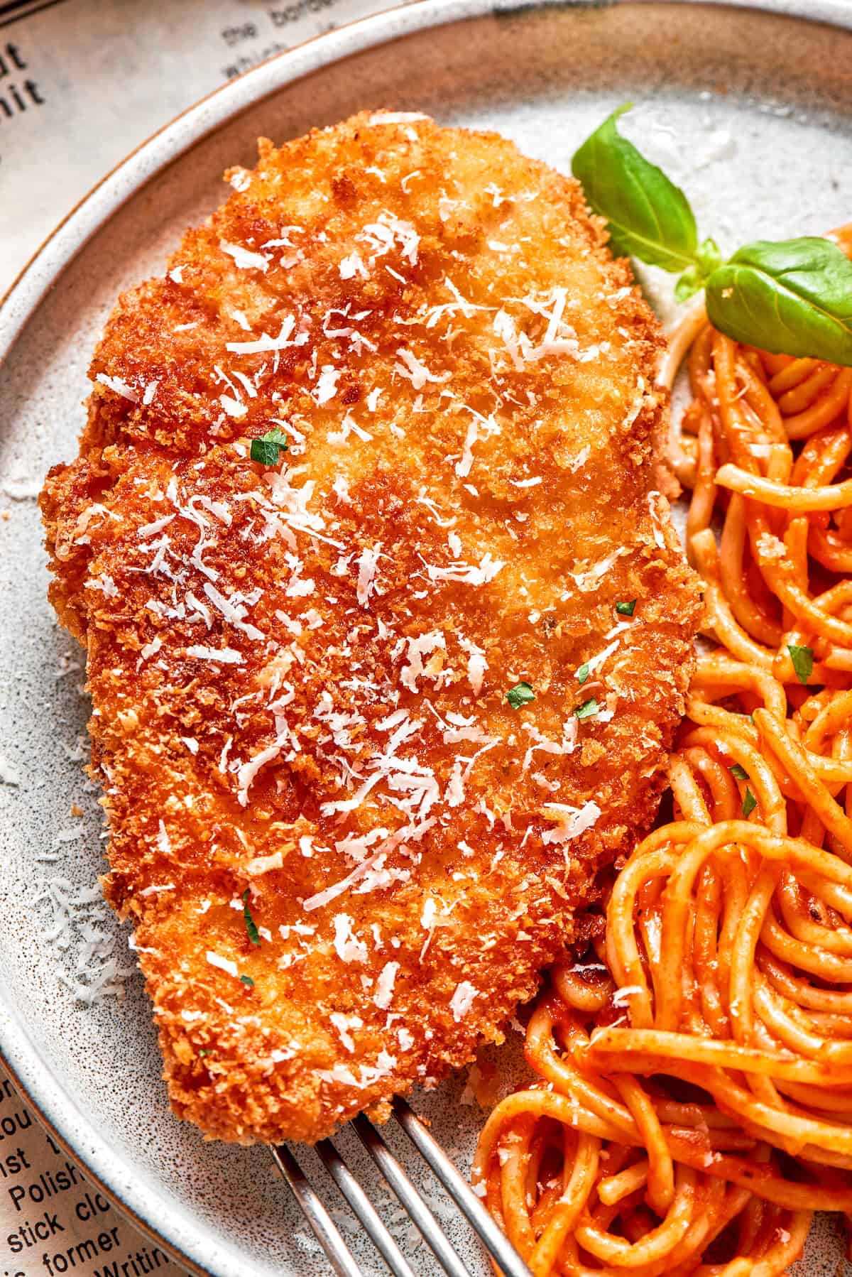 A big piece of crusted chicken romano served with spaghetti.