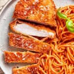 A piece of crusted chicken romano sliced and served with spaghetti.