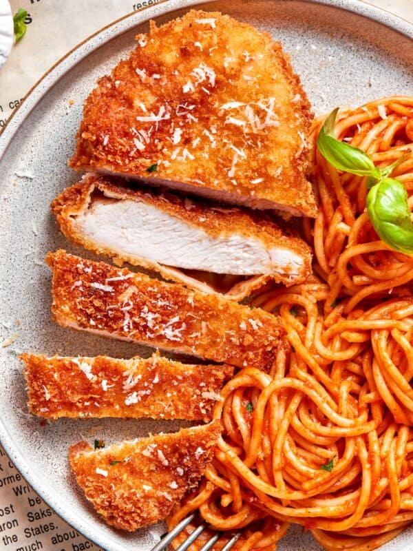 A piece of crusted chicken romano sliced and served with spaghetti.