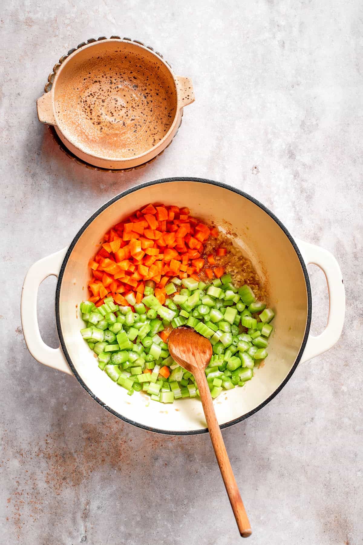 Celery and carrots are added to shallots in a pot.