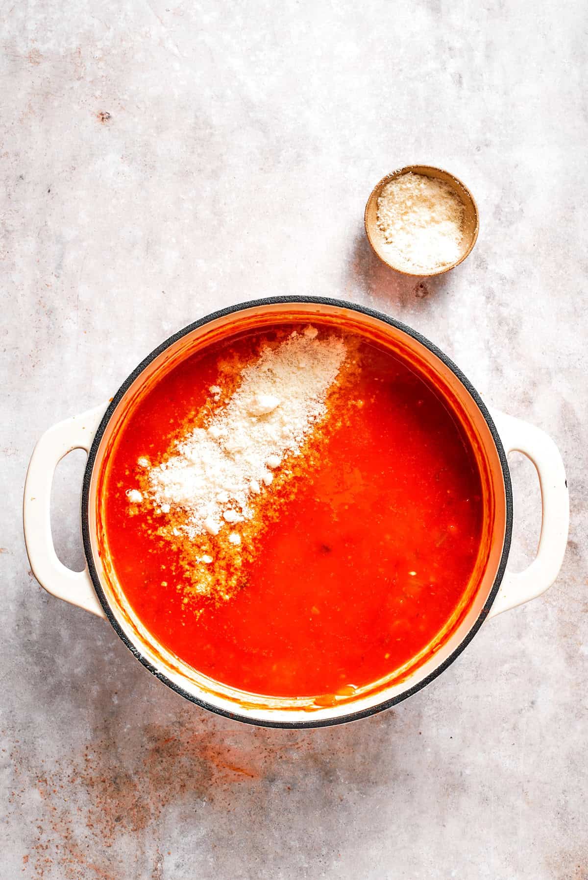 Parmesan cheese is added to a pot of tomato florentine soup.