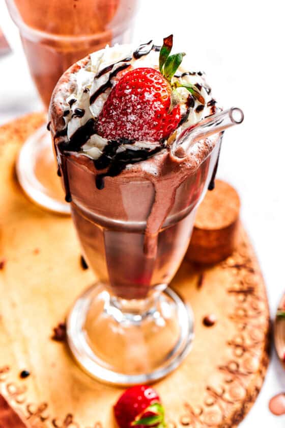 Chocolate milkshake served in a tall glass and garnished with whipped cream, strawberries, and a chocolate drizzle.