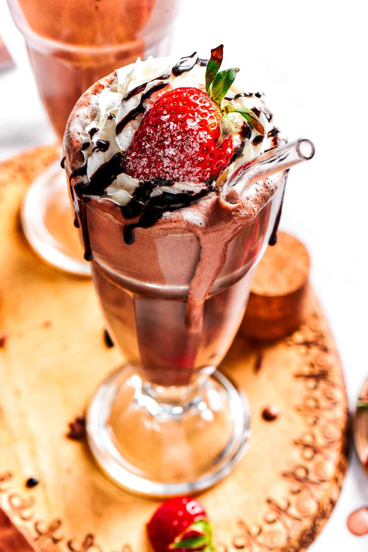 Chocolate milkshake served in a tall glass and garnished with whipped cream, strawberries, and a chocolate drizzle.