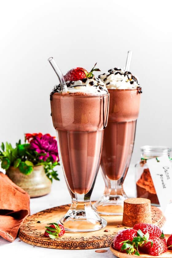 Chocolate milkshake served in tall glasses and garnished with whipped cream, strawberries, and a chocolate drizzle.