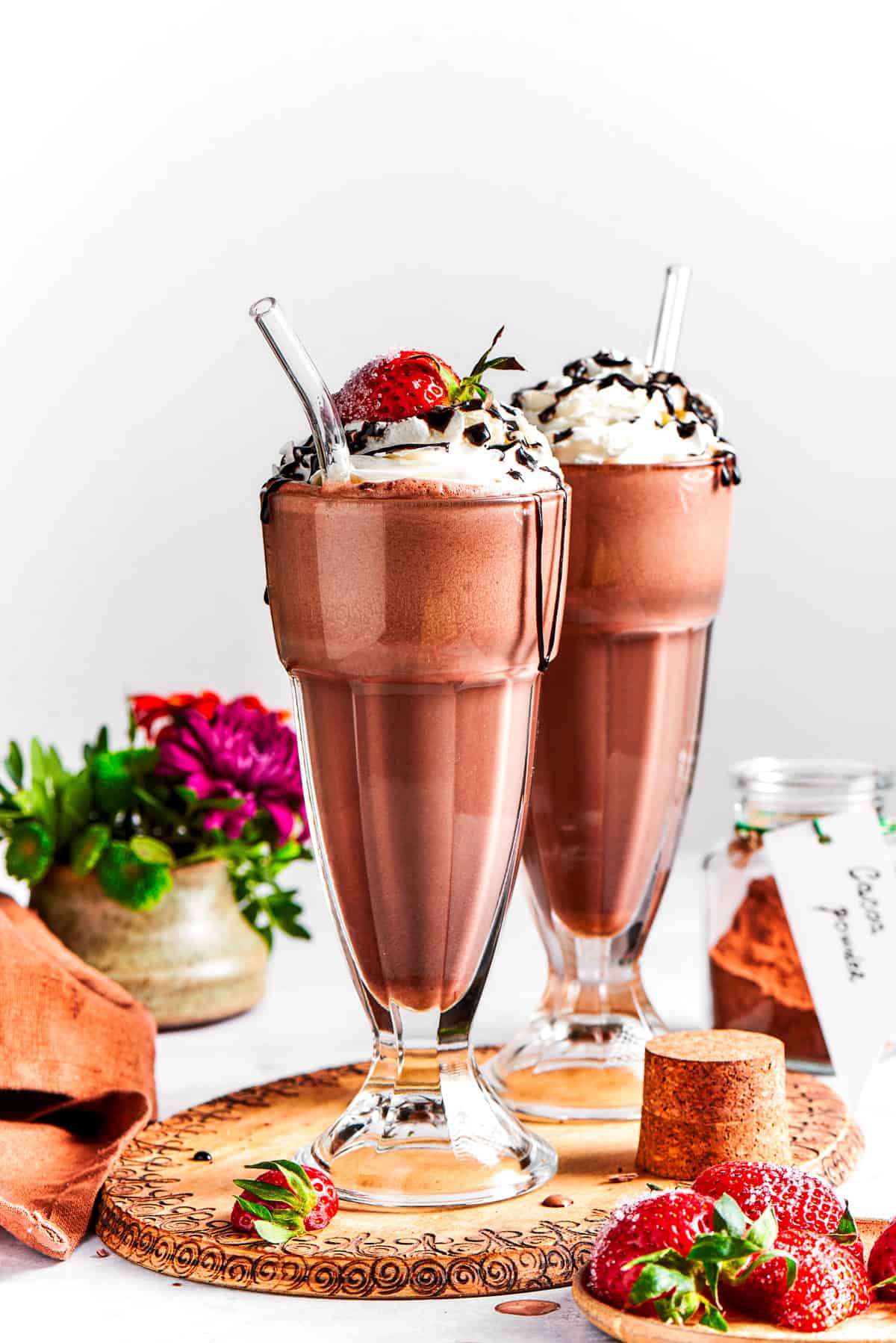Chocolate milkshake served in tall glasses and garnished with whipped cream, strawberries, and a chocolate drizzle.