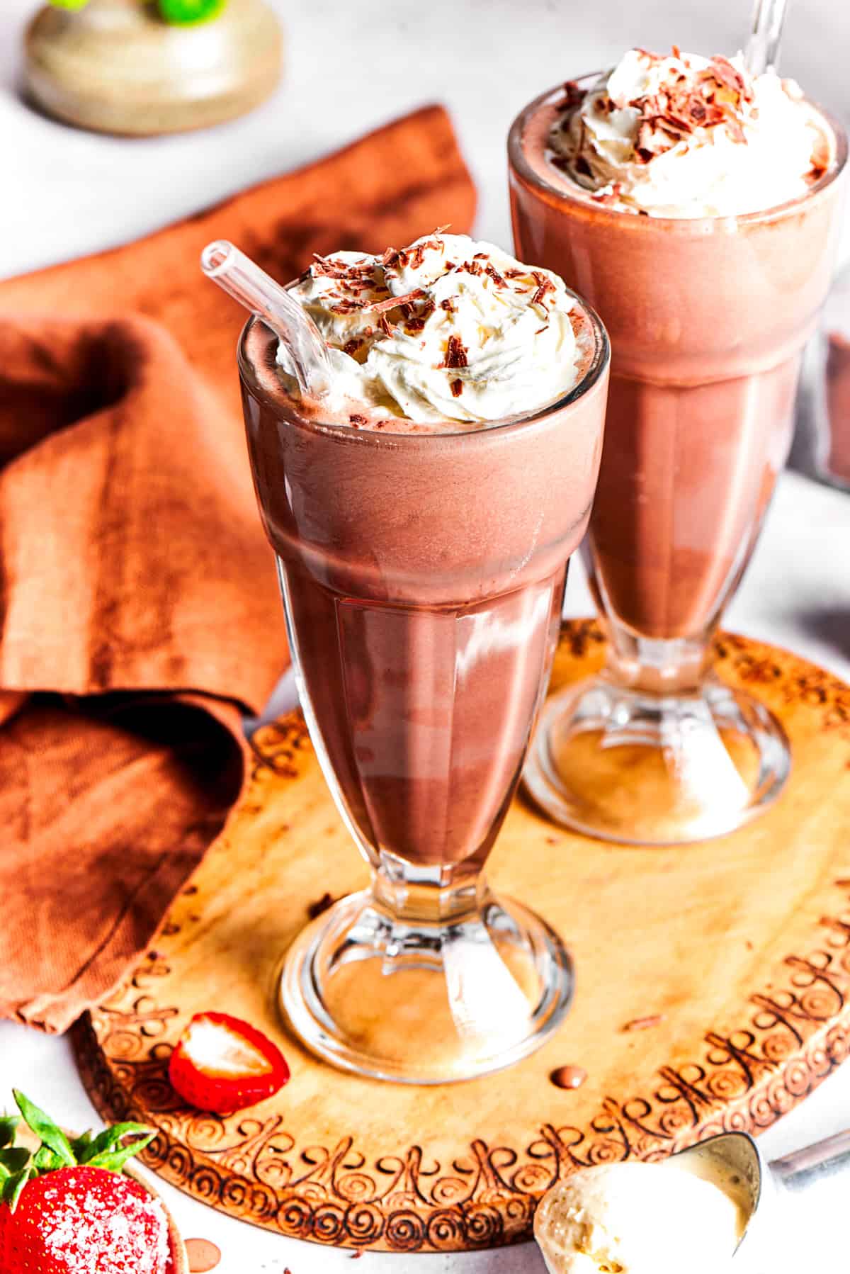 Two glasses of chocolate milkshake set on a wooden tray.