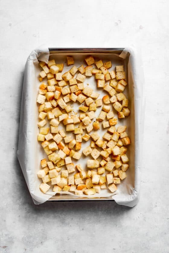 Homemade croutons cool on a lined baking sheet.