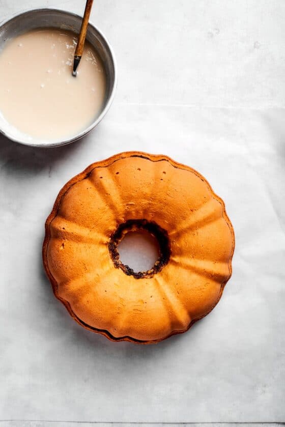 A bowl of icing next to a cooled cake.
