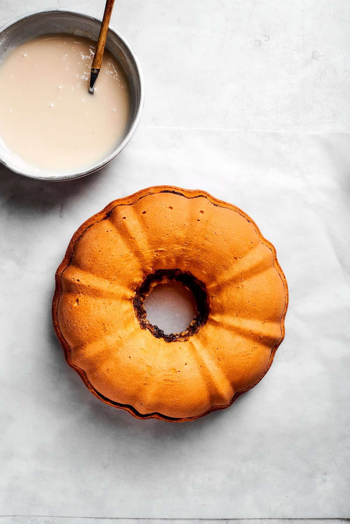 A bowl of icing next to a cooled cake.
