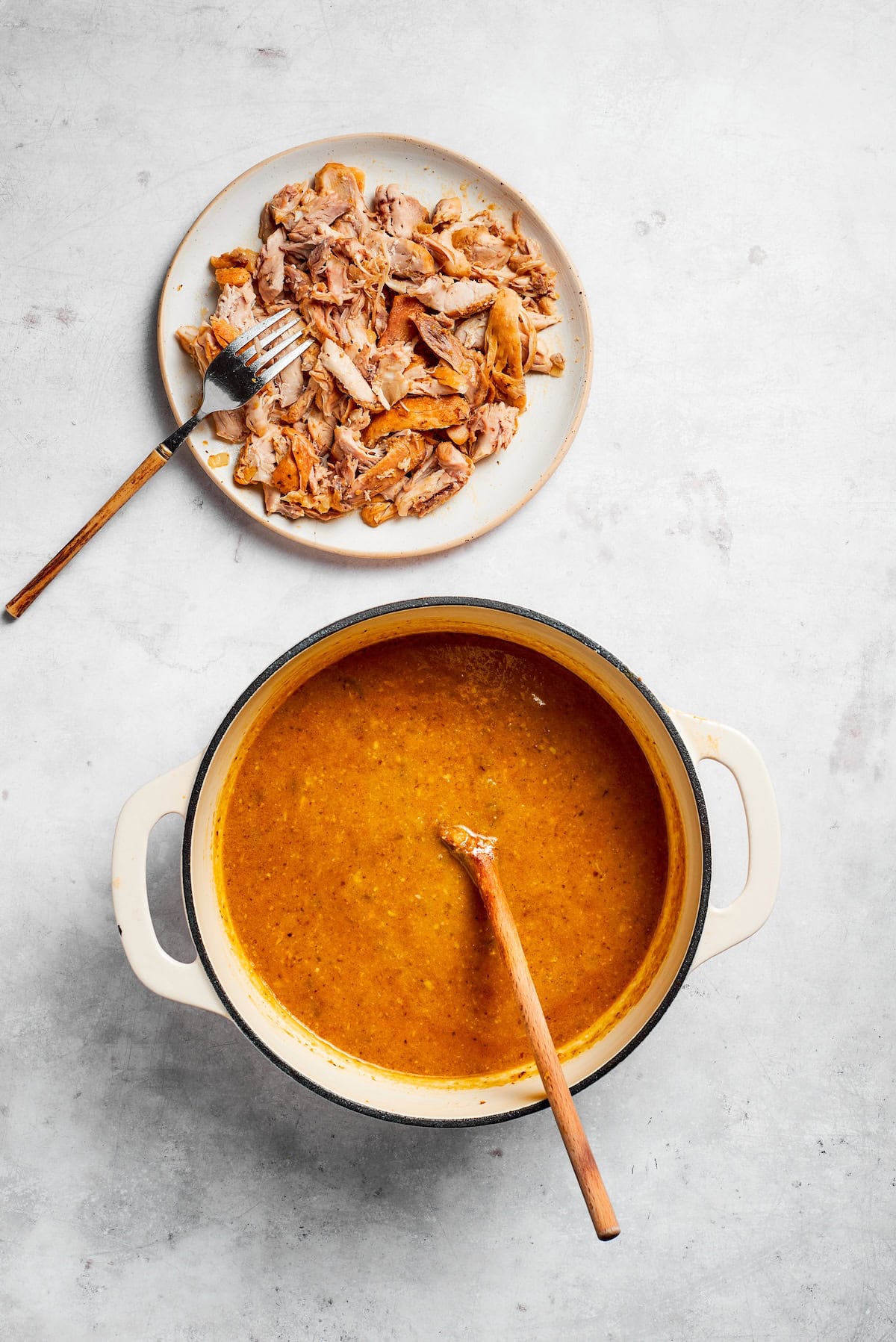A plate of shredded chicken next to a pot of soup.