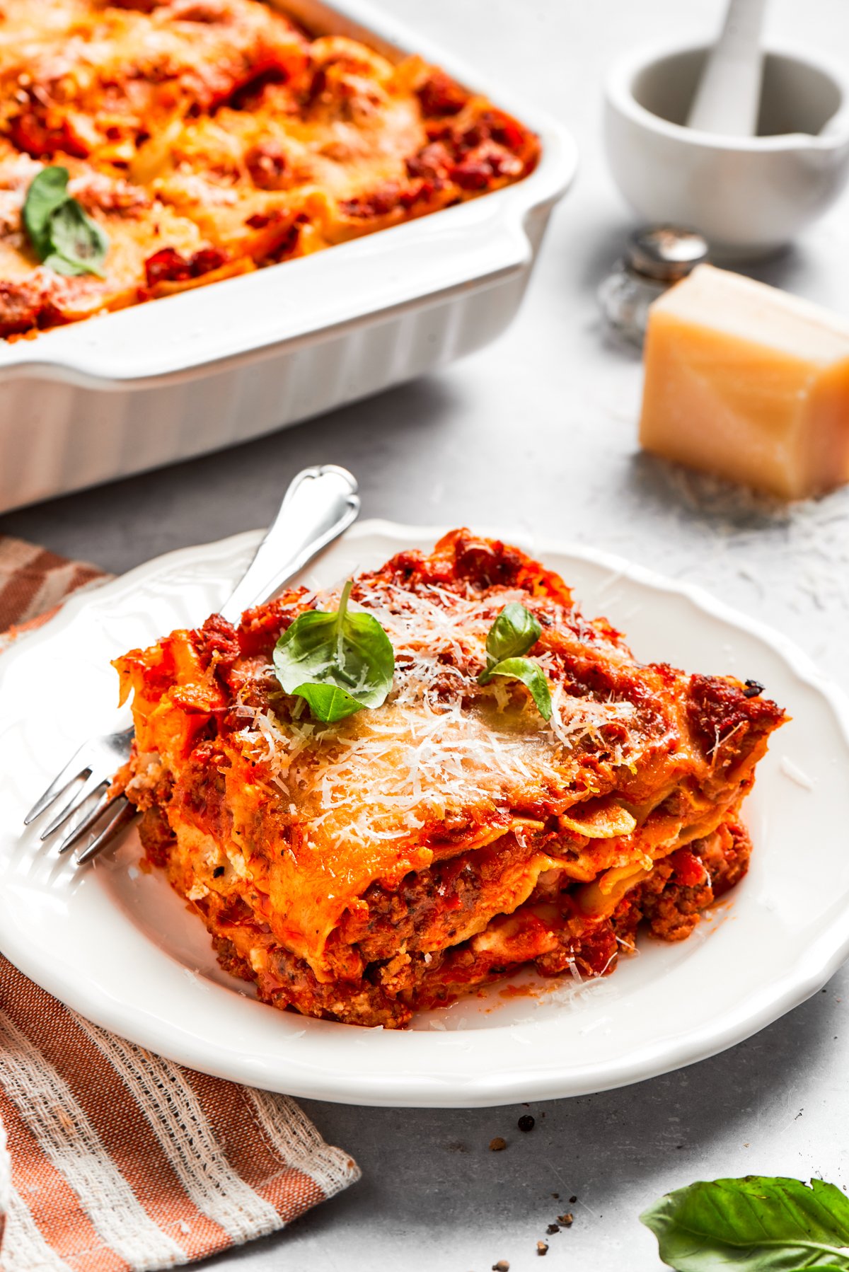 A serving of homemade beef lasagna served on a dinner plate with a fork.