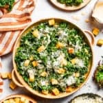 A large bowl of kale Caesar salad garnished with homemade croutons and shredded cheese.