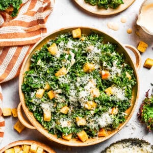 A large bowl of kale Caesar salad garnished with homemade croutons and shredded cheese.