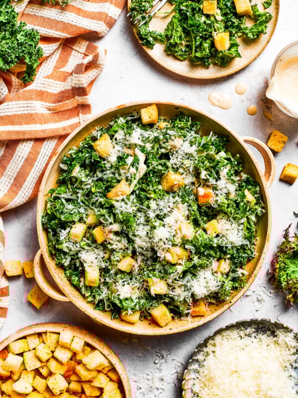 A large bowl of kale Caesar salad garnished with homemade croutons and shredded cheese.