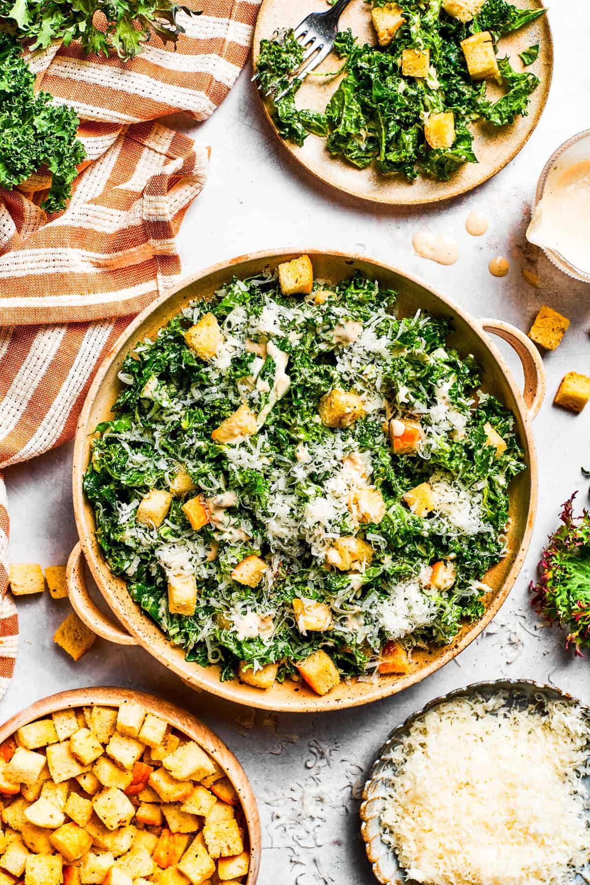 This kale Caesar salad recipe with homemade croutons is a twist on a classic Caesar with crisp toasted baguette slices and homemade dressing! A large bowl of kale Caesar salad garnished with homemade croutons and shredded cheese.