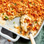 A serving spoon scooping out million dollar chicken casserole from a baking dish.