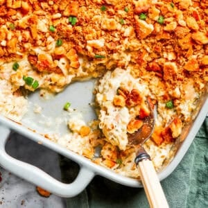 A serving spoon scooping out million dollar chicken casserole from a baking dish.