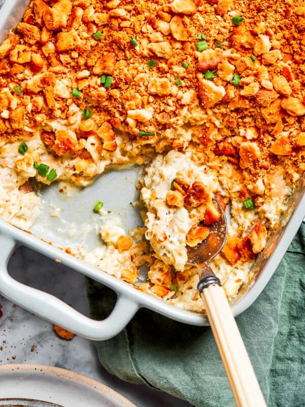 A serving spoon scooping out million dollar chicken casserole from a baking dish.