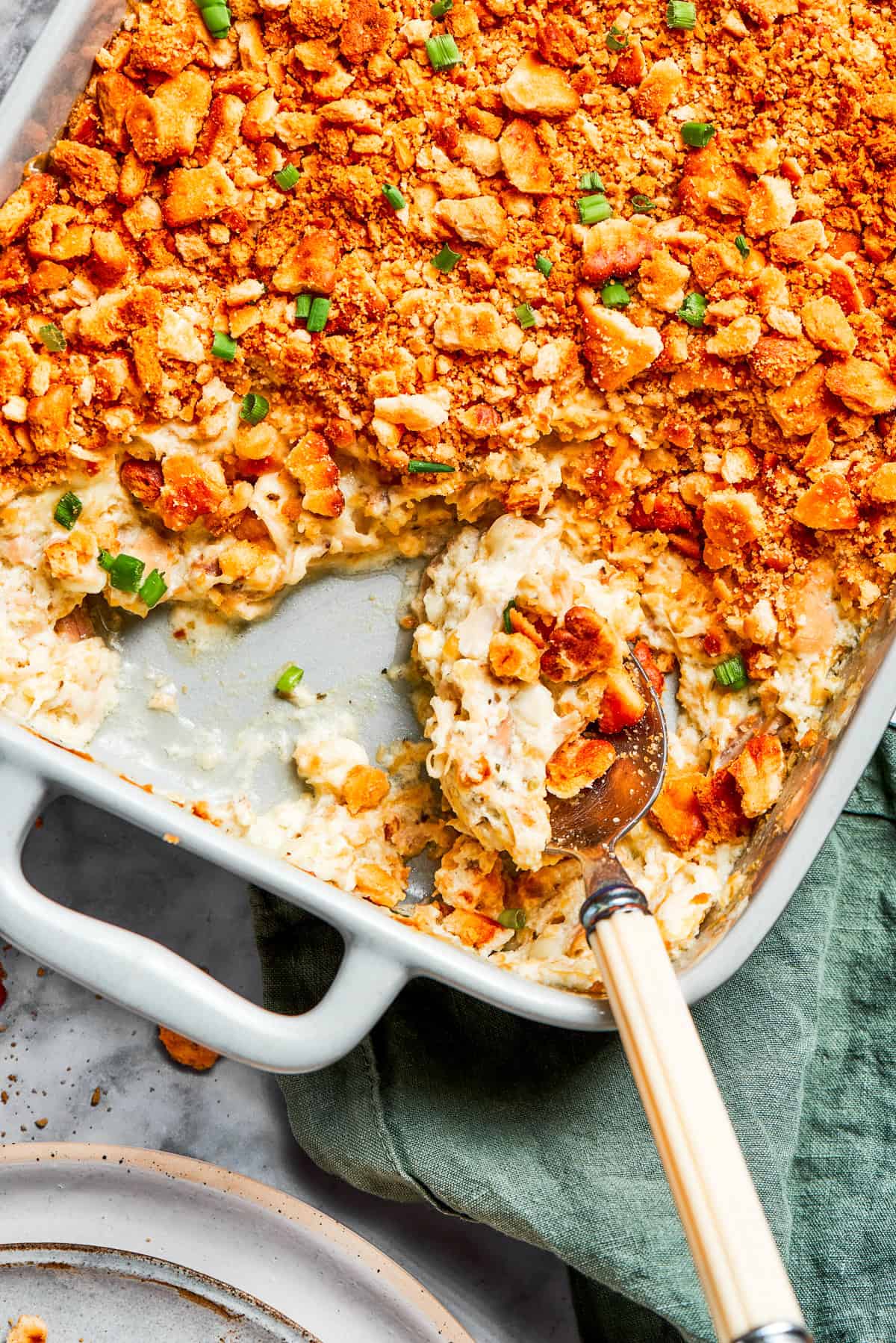This Million Dollar Chicken Casserole recipe features tender shredded chicken tossed in a creamy, cheesy sauce and topped with crushed Ritz crackers. A serving spoon scooping out million dollar chicken casserole from a baking dish.