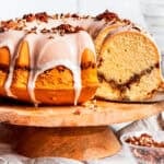 Sock it to me, cake served on a tall cake plate with a slice cut out exposing the cinnamon sugar ribbon that goes through the cake.