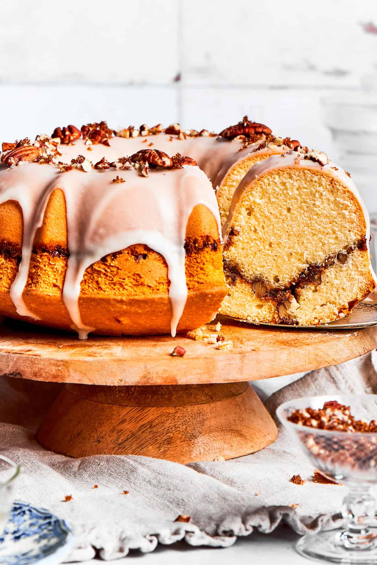 An easy recipe for Sock It To Me Cake, a tender coffee cake with a ribbon of brown sugar, cinnamon and toasted pecans through the center. Sock it to me, cake served on a tall cake plate with a slice cut out exposing the cinnamon sugar ribbon that goes through the cake.